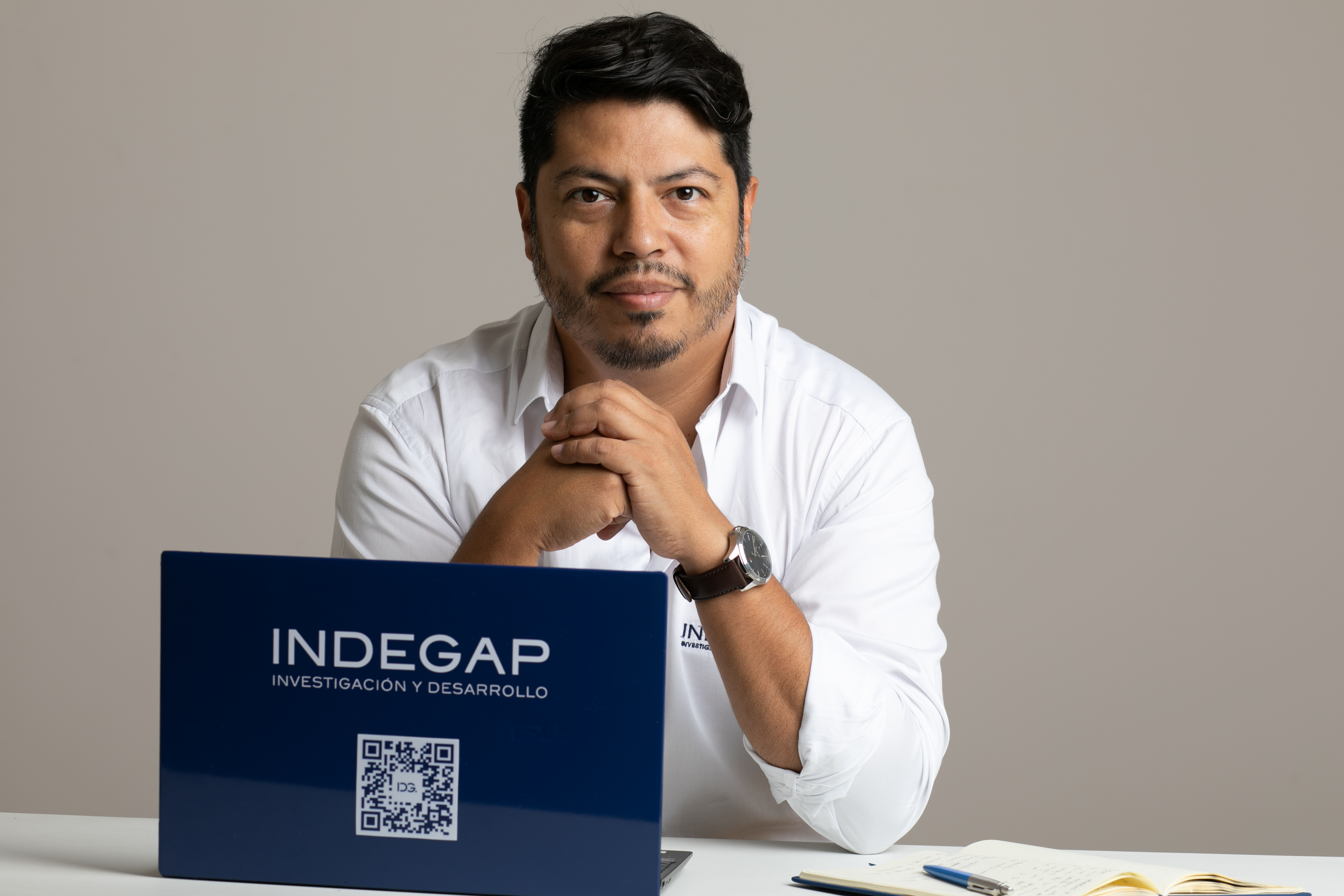 Hombre sentado frente a una computadora portátil con el logo de INDEGAP, gesto pensativo y expresión profesional, fondo neutro.